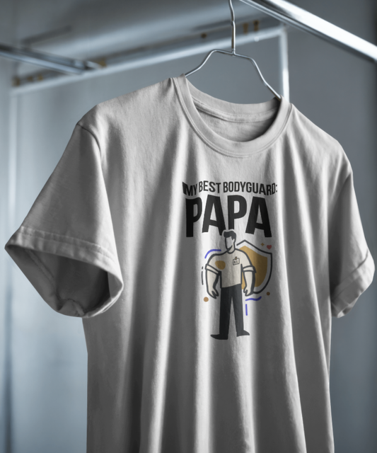 White graphic t-shirt featuring the text "MY BEST BODYGUARD: PAPA". The minimal design includes a creative illustration of a man standing confidently in front of a golden shield. Premium gifting and family streetwear by Nite Stream.